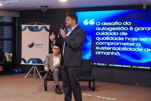 foto homem em pé falando ao microfone em frente a tela