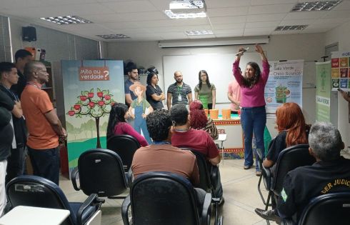 foto mulher em pé ministrando oficina; pessoas em pé e sentadas na plateia