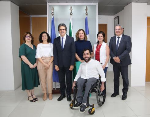 Fotografia de sete pessoas posando para foto em frente a bandeiras do Brasil, Pernambuco e Recife