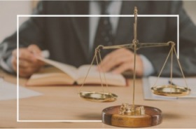 Imagem onde aparece uma balança, símbolo da Justiça, e ao fundo um homem de terno folheando um livro