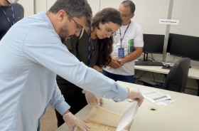 Fotografia onde aprecem quatro adultos manuseando um documento histórico