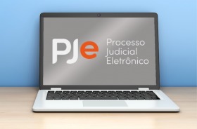 Arte mostra um notebook aberto e, na tela, tem a logo do sistema PJe
