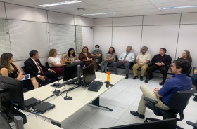 Fotografia onde aparece um grupo de 14 adultos sentados numa sala de audiências
