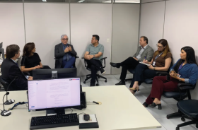 Fotografia de um grupo de sete adultos sentados numa sala de audiência