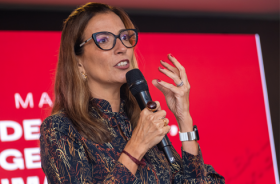 Fotografia onde aparece uma mulher, em close, durante apresentação de uma palestra