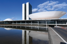 Foto mostra a fachada do Congresso Nacional, com dois prédios ao centro e um lago em primeiro plano