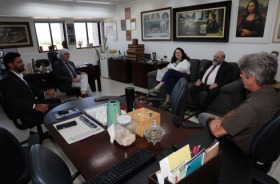 foto pessoas sentadas em cadeira e sofá reunidas em volta da mesa