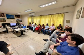 Na foto, aparece um grupo formado por 15 adultos sentados numa sala de audiência