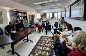 Fotografia onde aparece um grupo de 12 adultos sentados no gabinete da Corregedoria