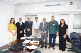 Sete pessoas posam para foto em sala de reuniões, ao lado de mesa com documentos