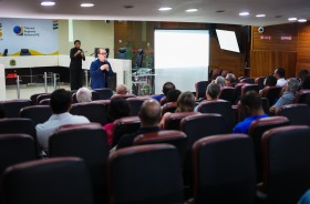 Foto mostra um auditório com um professor em pé, enquanto alunos sentados assistem