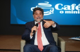 Fotografia onde aparece um senhor sentado palestrando com um microfone na mão