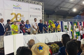 Fotografia onde aparecem vários adultos, perfilados diante de uma mesa de abertura, numa quadra de esportes