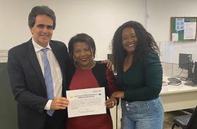 Fotografia onde aparecem três adultos segurando um certificado