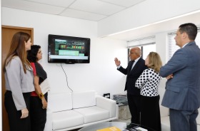 Foto mostra cinco adultos em pé, lado a lado, em frente a um painel interativo