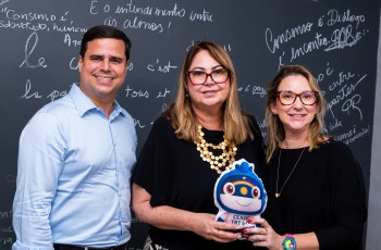 Fotografia onde aparecem um homem e duas mulheres perfilados, segurando um mascote