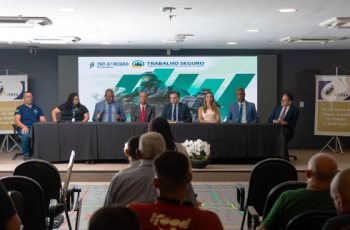 Fotografia onde aparecem oito adultos sentados numa mesa, diante de uma plateia