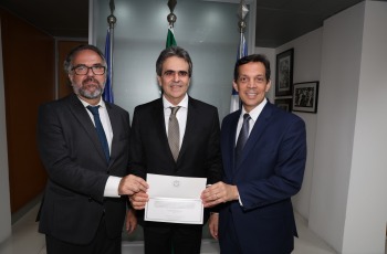 Na fotografia, três senhores de paletó seguram um convite