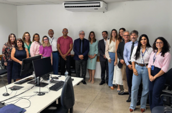 Fotografia onde aparece um grupo de 16 adultos perfilados numa sala de audiências