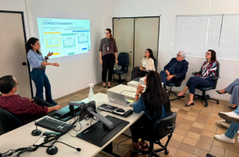 Fotografia onde aparecem duas mulheres de pé e um grupo de adultos sentados