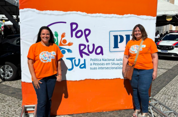 Fotografia onde aparecem duas mulheres perfiladas na frente de um banner